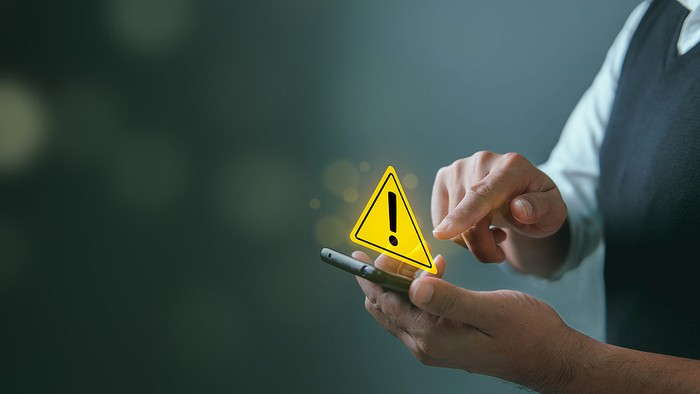 Man Using Smartphone with Warning Triangle